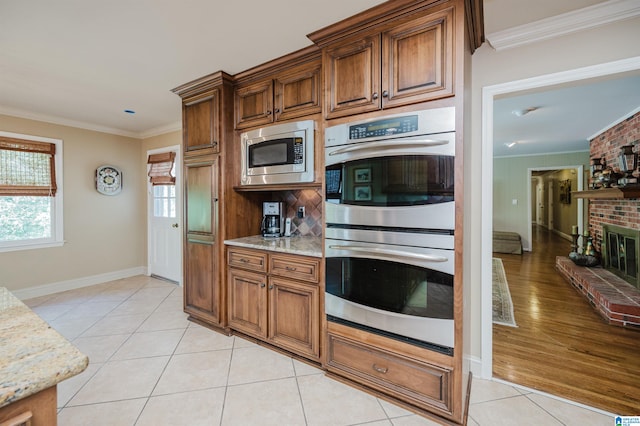 kitchen featuring light stone counters, ornamental molding, stainless steel appliances, a fireplace, and light wood-type flooring