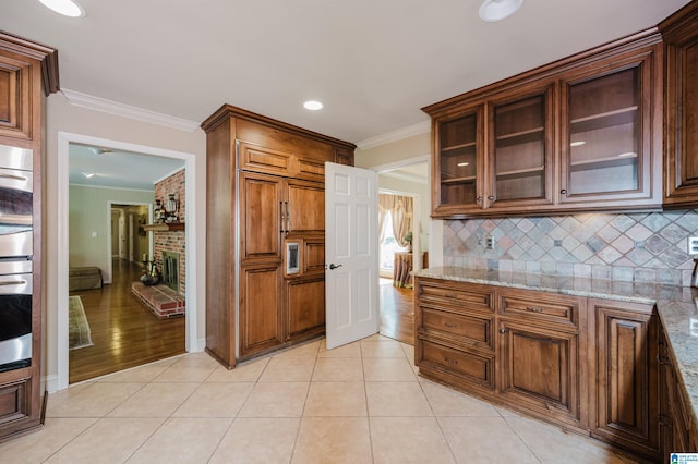 kitchen with light wood-type flooring, crown molding, backsplash, and light stone counters