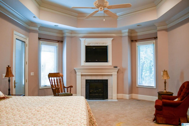 carpeted bedroom featuring crown molding, a tray ceiling, a tile fireplace, and ceiling fan