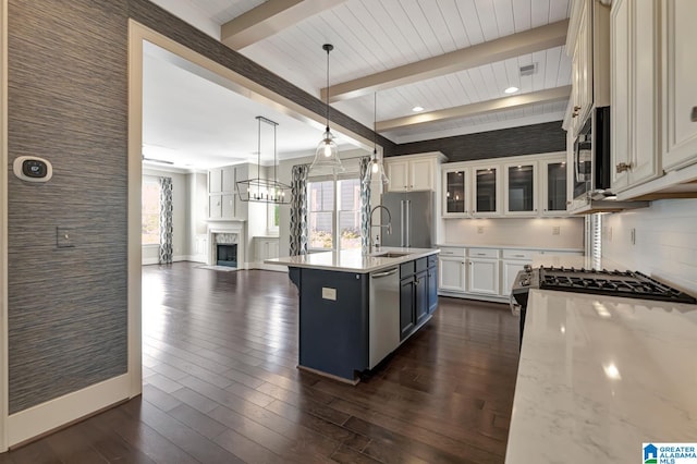 kitchen with appliances with stainless steel finishes, beam ceiling, an island with sink, and dark hardwood / wood-style flooring