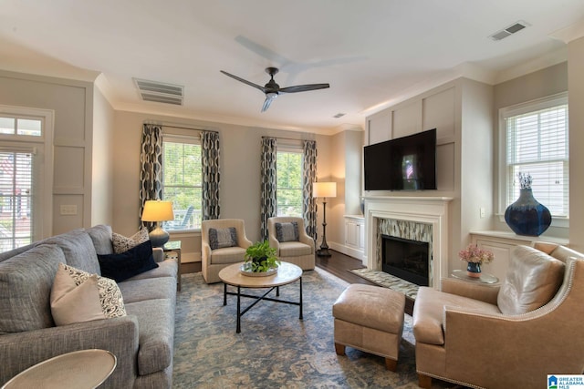 living room with dark wood-type flooring, ornamental molding, ceiling fan, and a healthy amount of sunlight