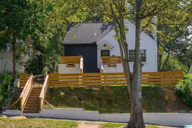 view of front of home with a shingled roof, fence, and stairs