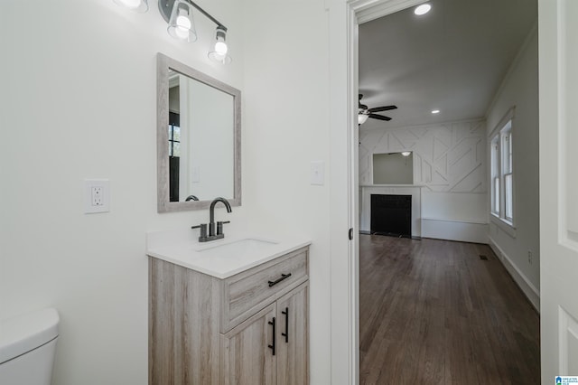 bathroom featuring ceiling fan, vanity, a large fireplace, toilet, and wood finished floors