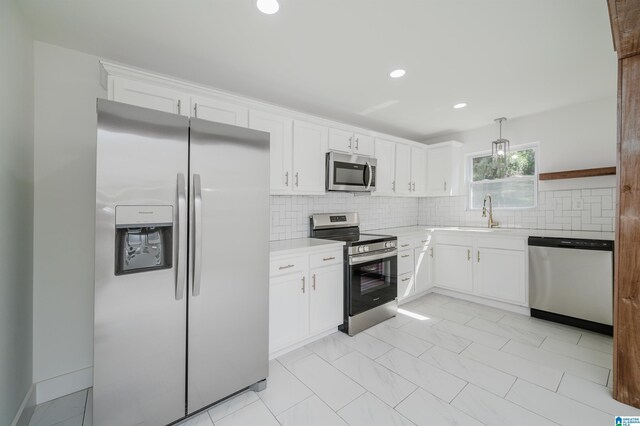 kitchen featuring white cabinets, appliances with stainless steel finishes, light countertops, a sink, and backsplash