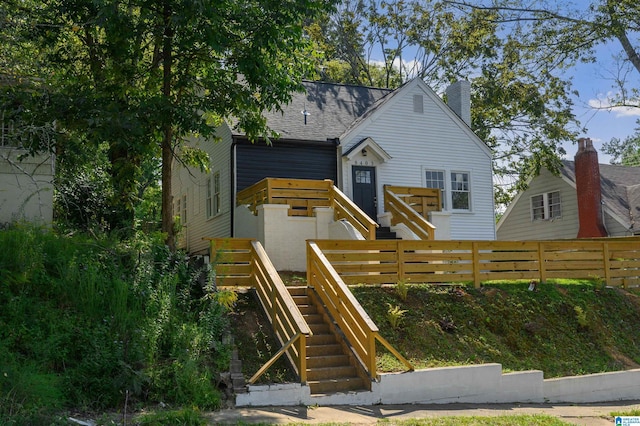 view of front of house featuring a wooden deck, stairway, roof with shingles, fence, and a chimney