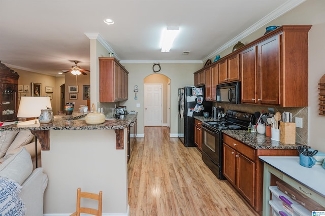 kitchen featuring black appliances, dark stone countertops, crown molding, and a breakfast bar