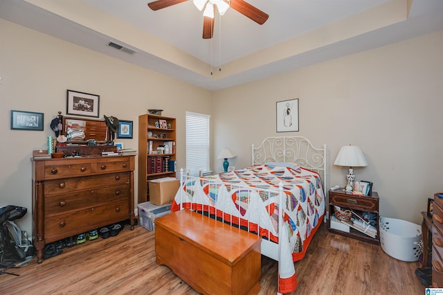 bedroom with light hardwood / wood-style floors, a tray ceiling, and ceiling fan