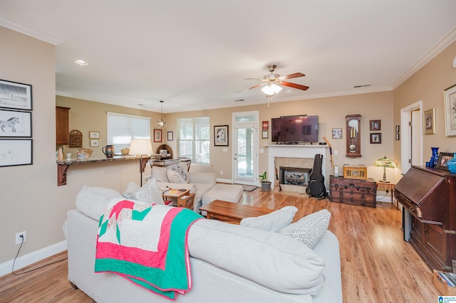 living room with light wood-type flooring, ceiling fan, crown molding, and a fireplace