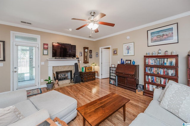 living room with ceiling fan, a tile fireplace, light hardwood / wood-style floors, and crown molding