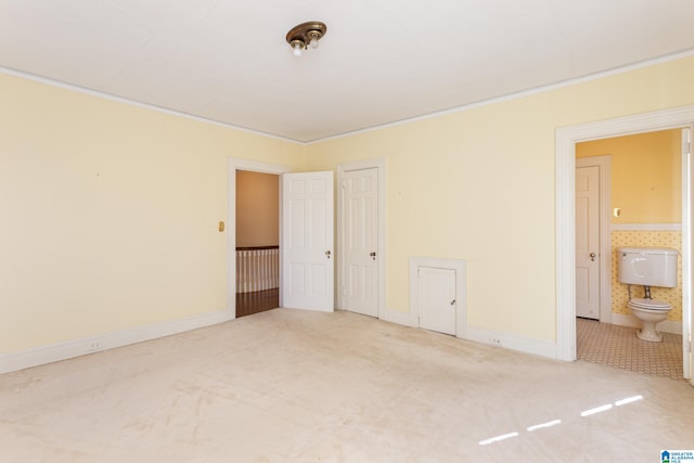 unfurnished bedroom featuring ornamental molding, ensuite bathroom, and carpet