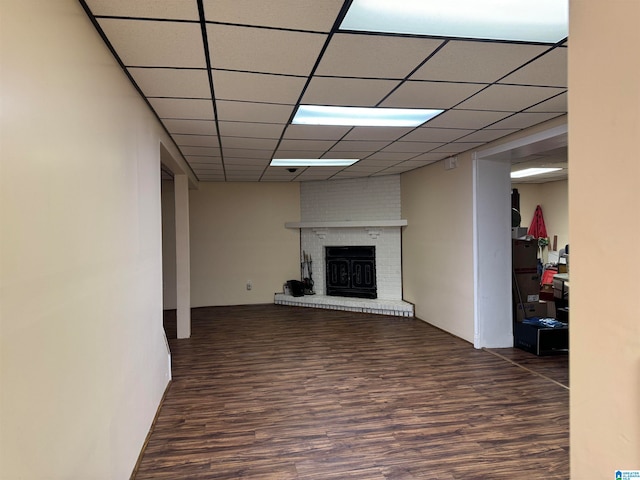 unfurnished living room with a brick fireplace, a drop ceiling, and dark hardwood / wood-style floors