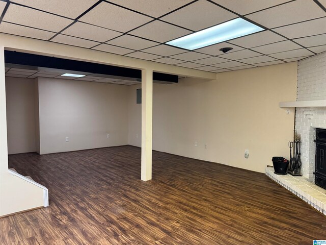 basement featuring a drop ceiling, dark wood-type flooring, and a wood stove