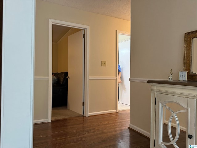 hallway with a textured ceiling, ornamental molding, and dark wood-type flooring