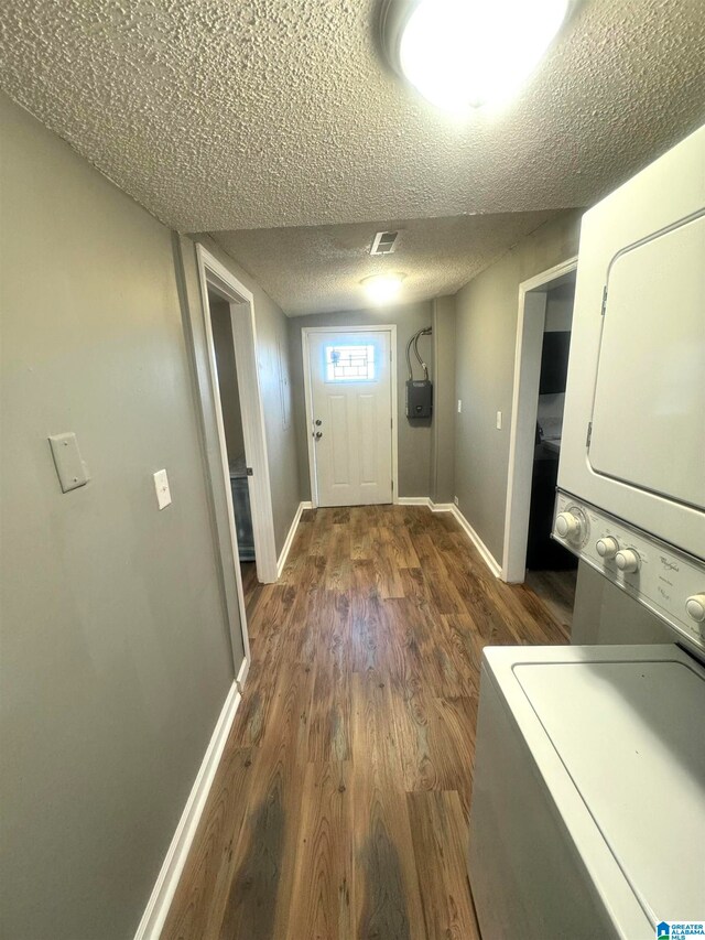 washroom with stacked washer and dryer, a textured ceiling, and dark hardwood / wood-style floors