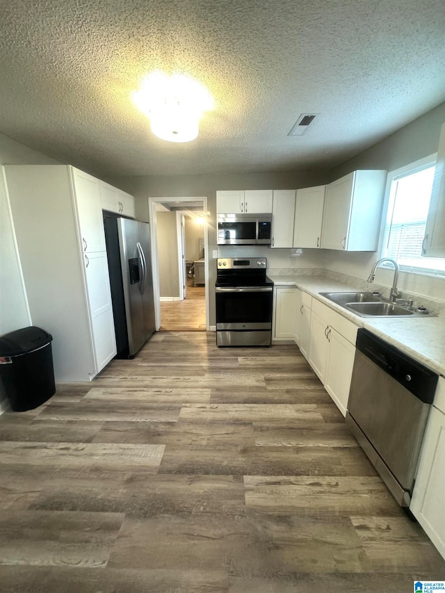 kitchen with white cabinets, stainless steel appliances, a textured ceiling, light hardwood / wood-style flooring, and sink