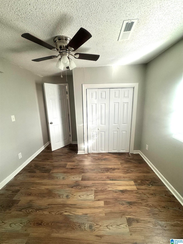 unfurnished bedroom with ceiling fan, a textured ceiling, a closet, and dark hardwood / wood-style flooring