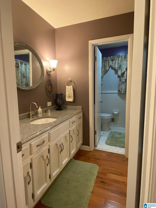 bathroom with toilet, vanity, wood finished floors, and a textured ceiling
