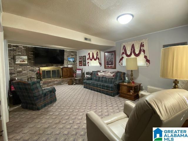 carpeted living area with visible vents, a textured ceiling, and a brick fireplace