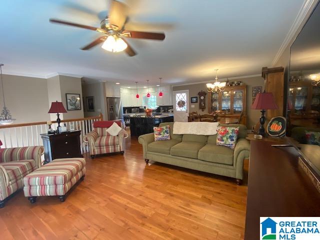 living room with ceiling fan with notable chandelier, ornamental molding, and light hardwood / wood-style flooring