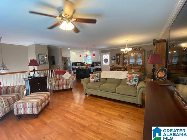 living area with ceiling fan with notable chandelier, light wood finished floors, and ornamental molding