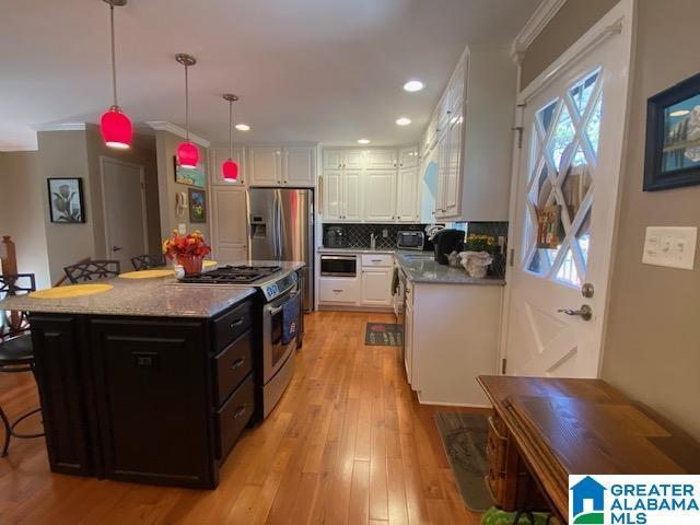 kitchen featuring white cabinets, light wood-type flooring, a breakfast bar, crown molding, and stainless steel appliances