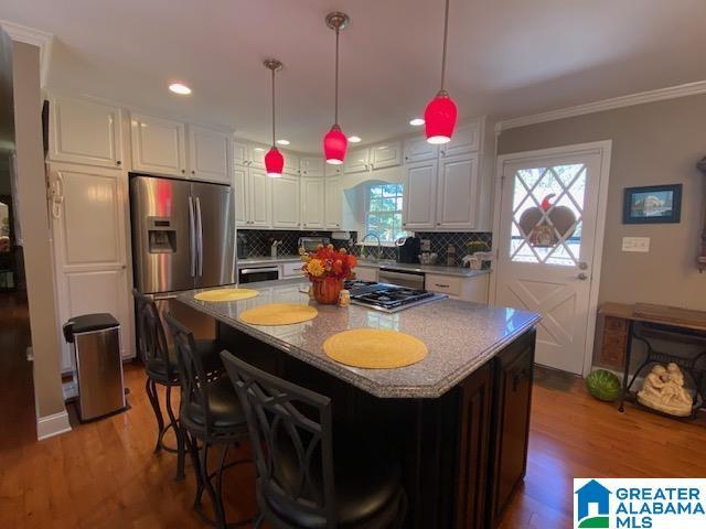 kitchen with stainless steel fridge with ice dispenser, crown molding, white cabinetry, wood finished floors, and decorative backsplash