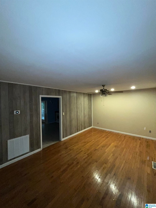 unfurnished room featuring wood-type flooring, wood walls, and ceiling fan