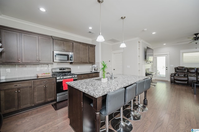 kitchen with an island with sink, ornamental molding, appliances with stainless steel finishes, and dark wood-type flooring