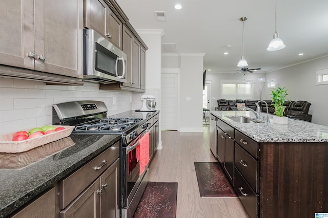 kitchen featuring light wood-type flooring, stainless steel appliances, ornamental molding, dark stone countertops, and ceiling fan