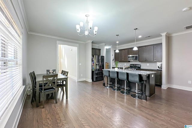 kitchen featuring hanging light fixtures, dark hardwood / wood-style flooring, stainless steel appliances, dark brown cabinets, and a kitchen island with sink