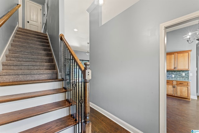 stairs with wood-type flooring and an inviting chandelier