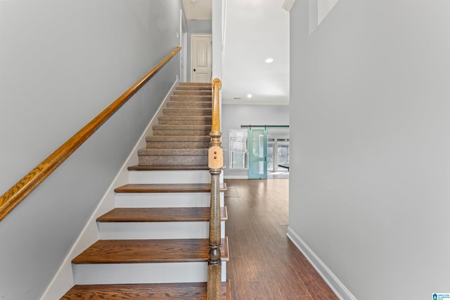 stairway with wood-type flooring, crown molding, and a barn door