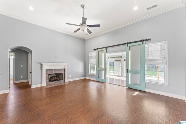 unfurnished living room featuring a barn door, ornamental molding, dark hardwood / wood-style floors, and ceiling fan