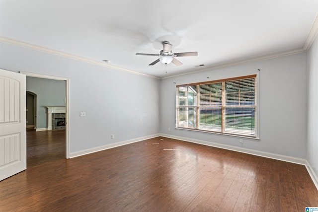 empty room with ceiling fan, a fireplace, dark wood-type flooring, and crown molding