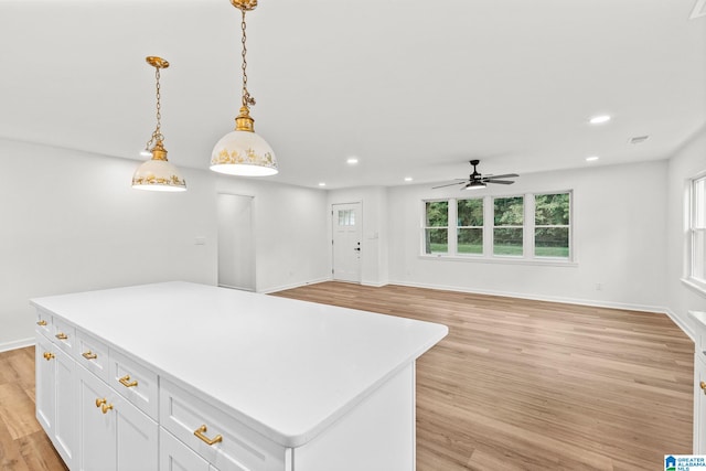 kitchen featuring ceiling fan, white cabinets, pendant lighting, a kitchen island, and light hardwood / wood-style floors