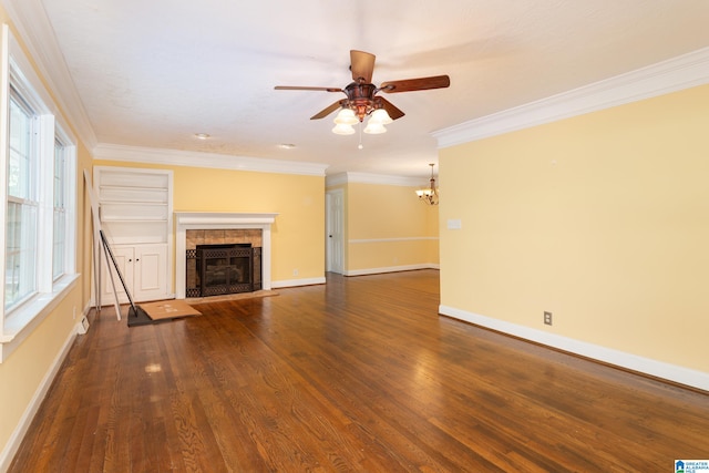 unfurnished living room featuring ornamental molding, ceiling fan with notable chandelier, a tiled fireplace, and dark hardwood / wood-style flooring