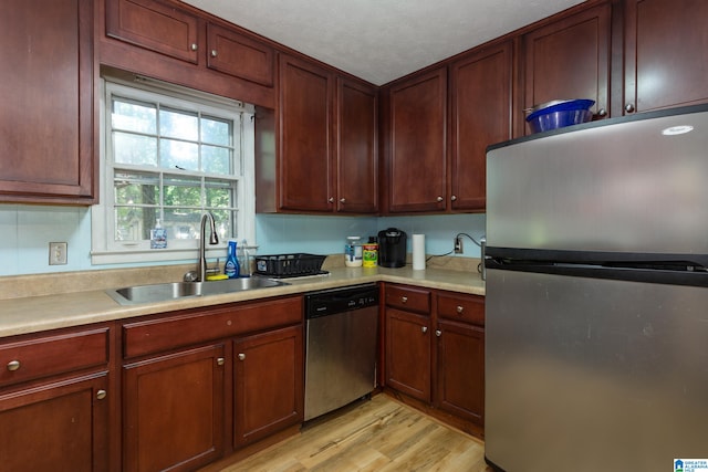 kitchen featuring appliances with stainless steel finishes, a textured ceiling, sink, and light hardwood / wood-style flooring