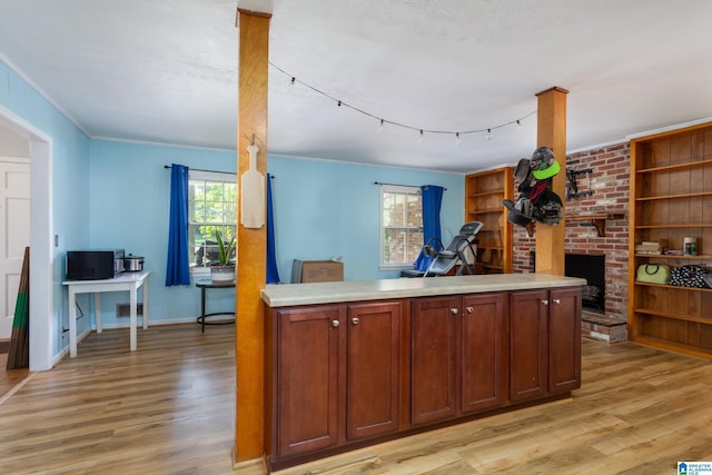 kitchen with a brick fireplace, light hardwood / wood-style floors, a textured ceiling, and crown molding