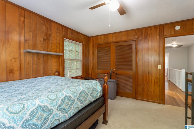 bedroom with a closet, wood walls, ceiling fan, and light colored carpet