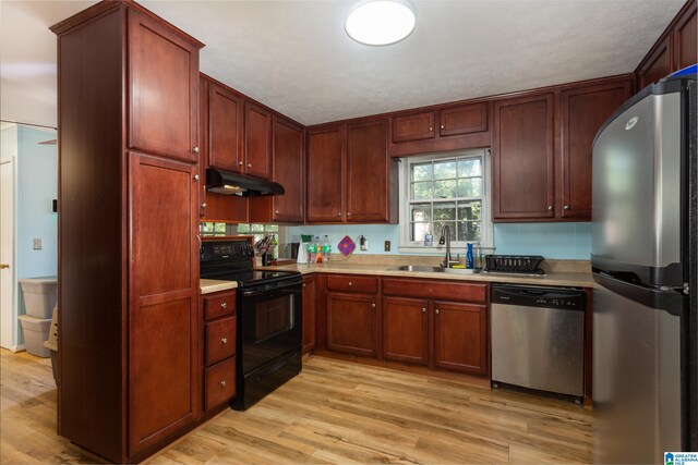 kitchen with a textured ceiling, appliances with stainless steel finishes, sink, and light hardwood / wood-style flooring