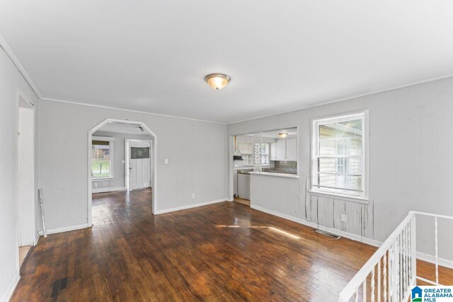 unfurnished living room featuring dark wood-type flooring and crown molding