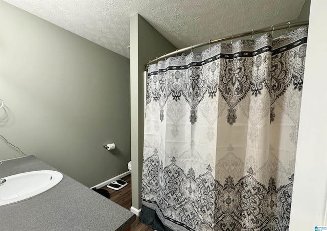 bathroom with a textured ceiling, hardwood / wood-style floors, a shower with shower curtain, toilet, and sink