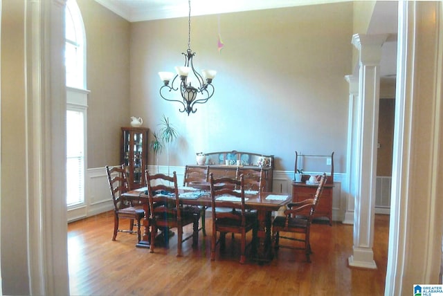 dining space with wood-type flooring, an inviting chandelier, ornate columns, and ornamental molding