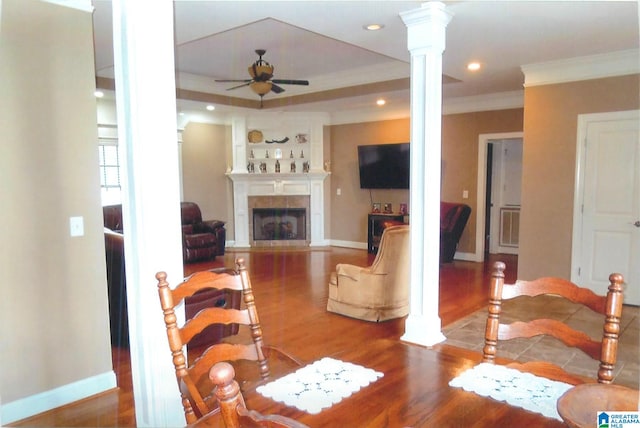 living room featuring a tile fireplace, decorative columns, hardwood / wood-style floors, crown molding, and ceiling fan