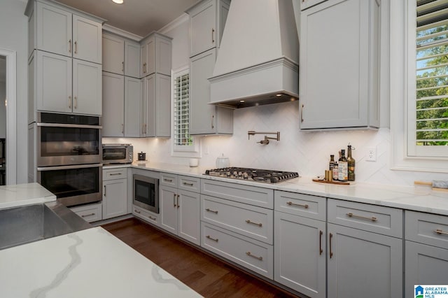 kitchen with dark hardwood / wood-style floors, light stone countertops, appliances with stainless steel finishes, tasteful backsplash, and custom range hood