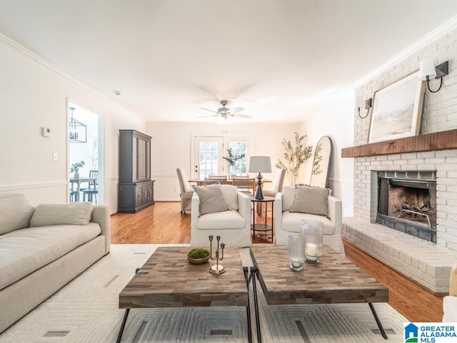 living room featuring a brick fireplace, crown molding, light hardwood / wood-style floors, and ceiling fan