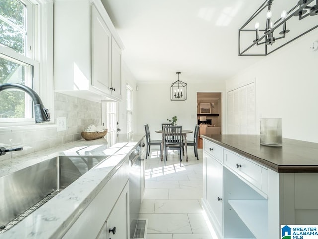 kitchen with tasteful backsplash, sink, white cabinetry, hanging light fixtures, and stainless steel dishwasher