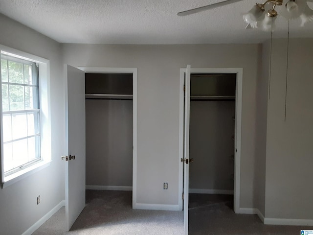 unfurnished bedroom featuring ceiling fan, a textured ceiling, two closets, and carpet