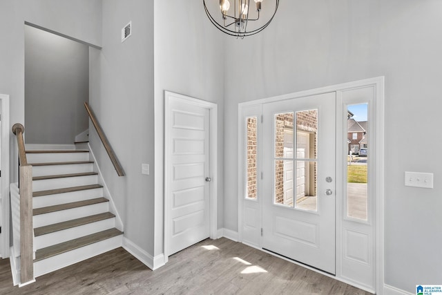 foyer with a towering ceiling, baseboards, an inviting chandelier, stairway, and wood finished floors