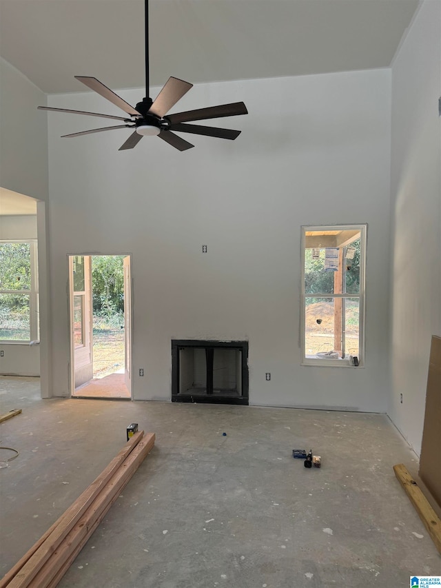 unfurnished living room featuring ceiling fan, a healthy amount of sunlight, and a high ceiling